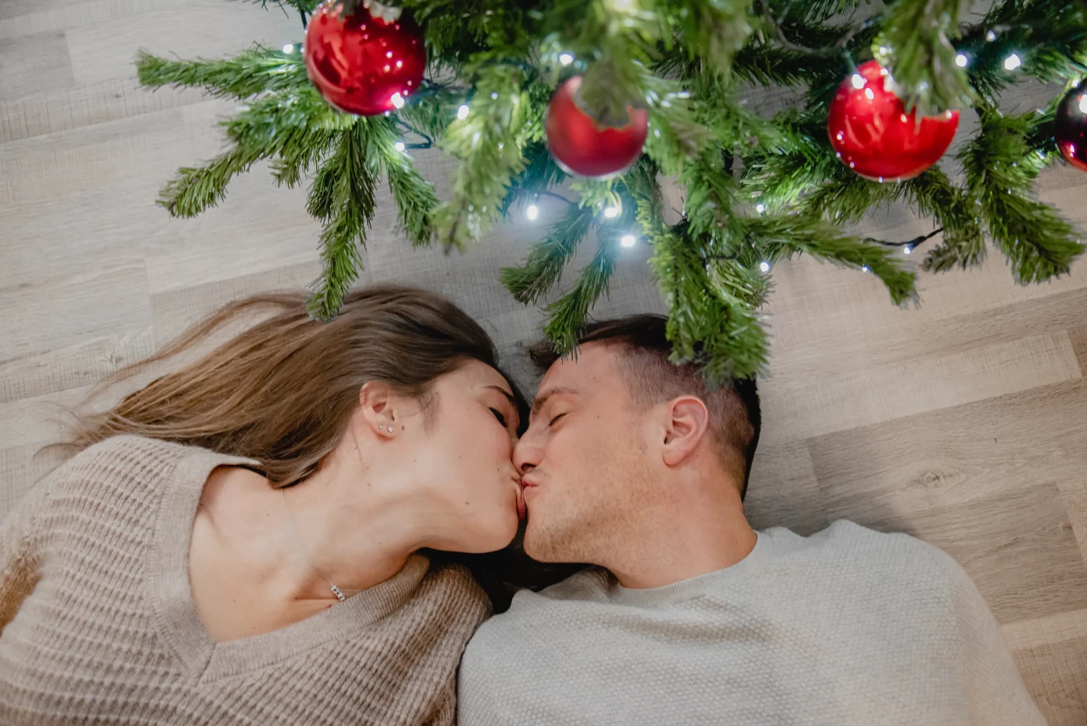 Una coppia sdraiata sul pavimento di casa si bacia tra i rami di Natale